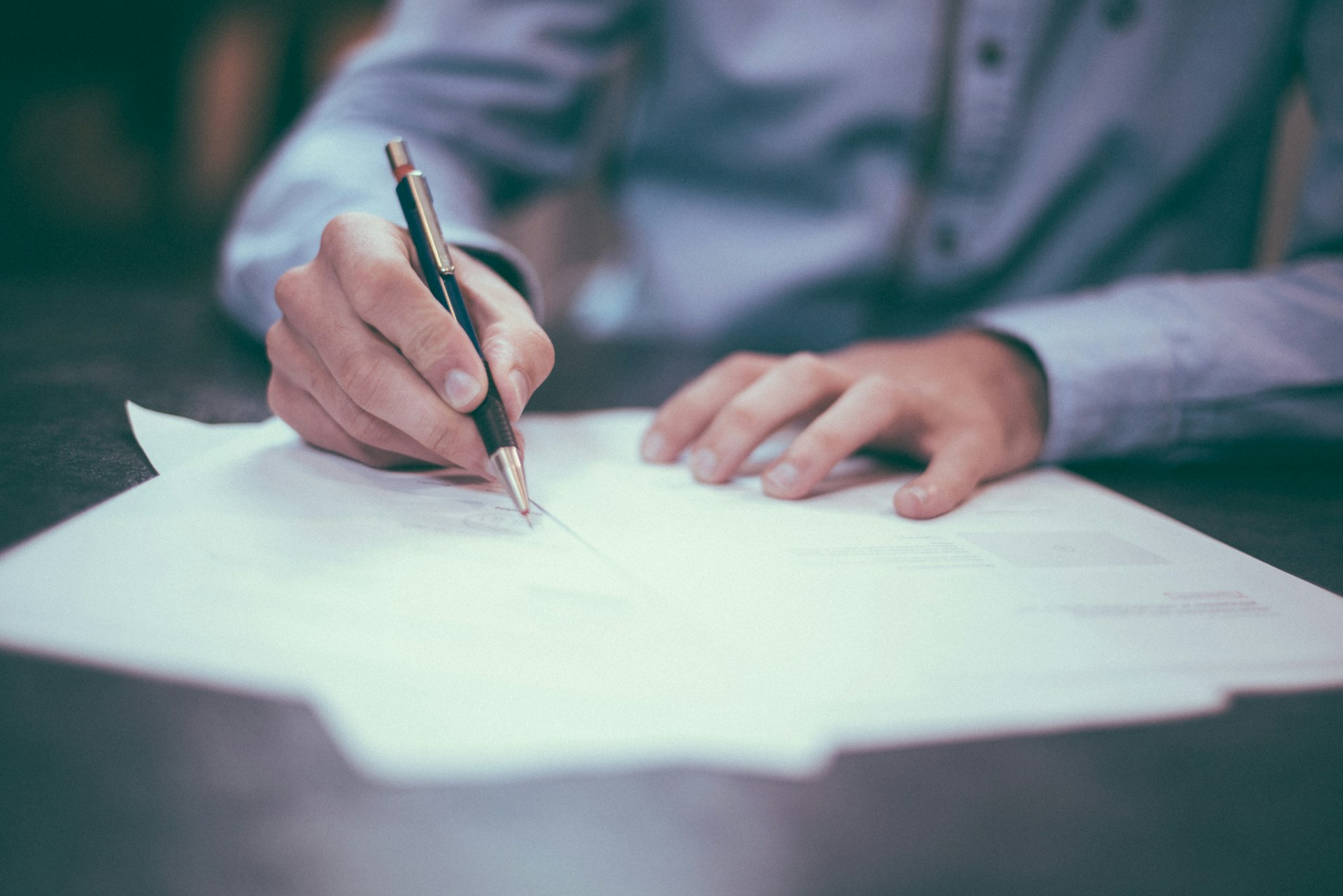 Man signing paperwork spread on a desk in front of him with a pen