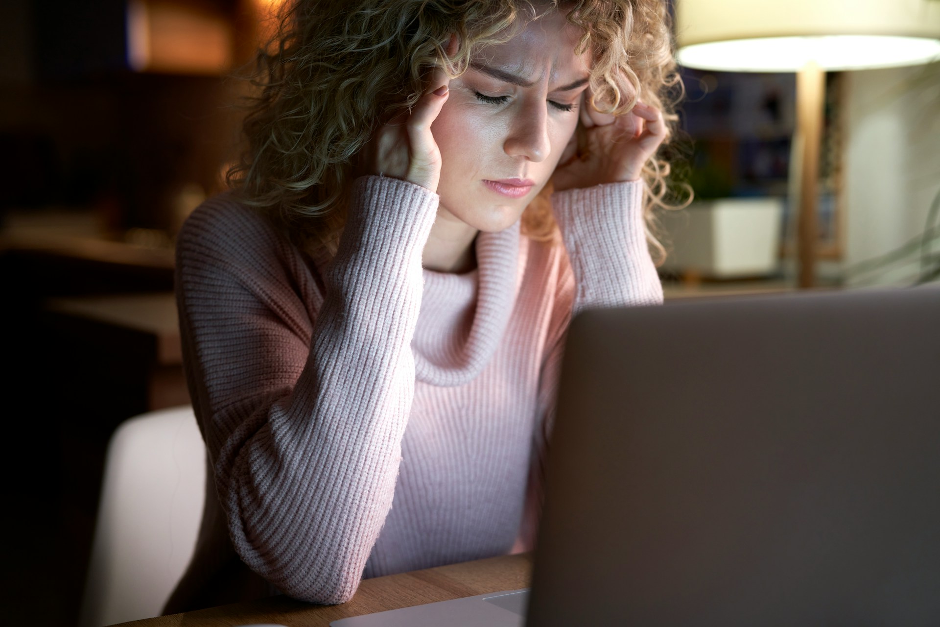 Woman in front of a laptop with her eyes closed and her hands on her temples in exhaustion